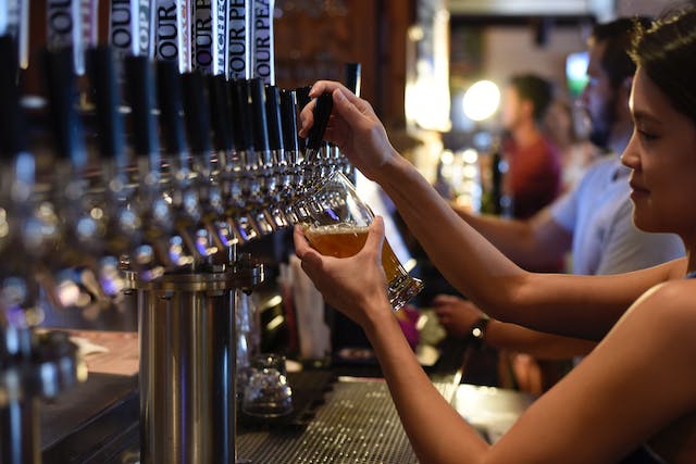 Lady at a bar pooring a glass of beer