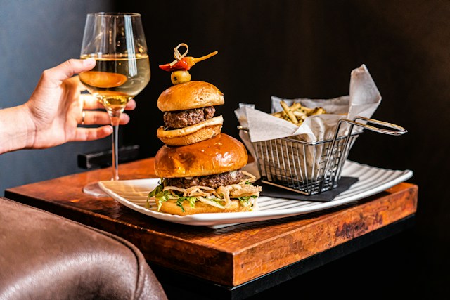 A woman drinking wine and eating burger & french fries